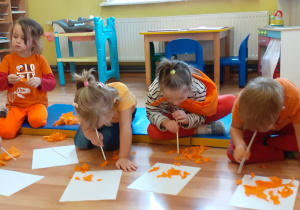 Ćwiczenia oddechowe: 4 dzieci przenosi za pomocą słomki skrawki pomarańczowej bibuły na kartony.